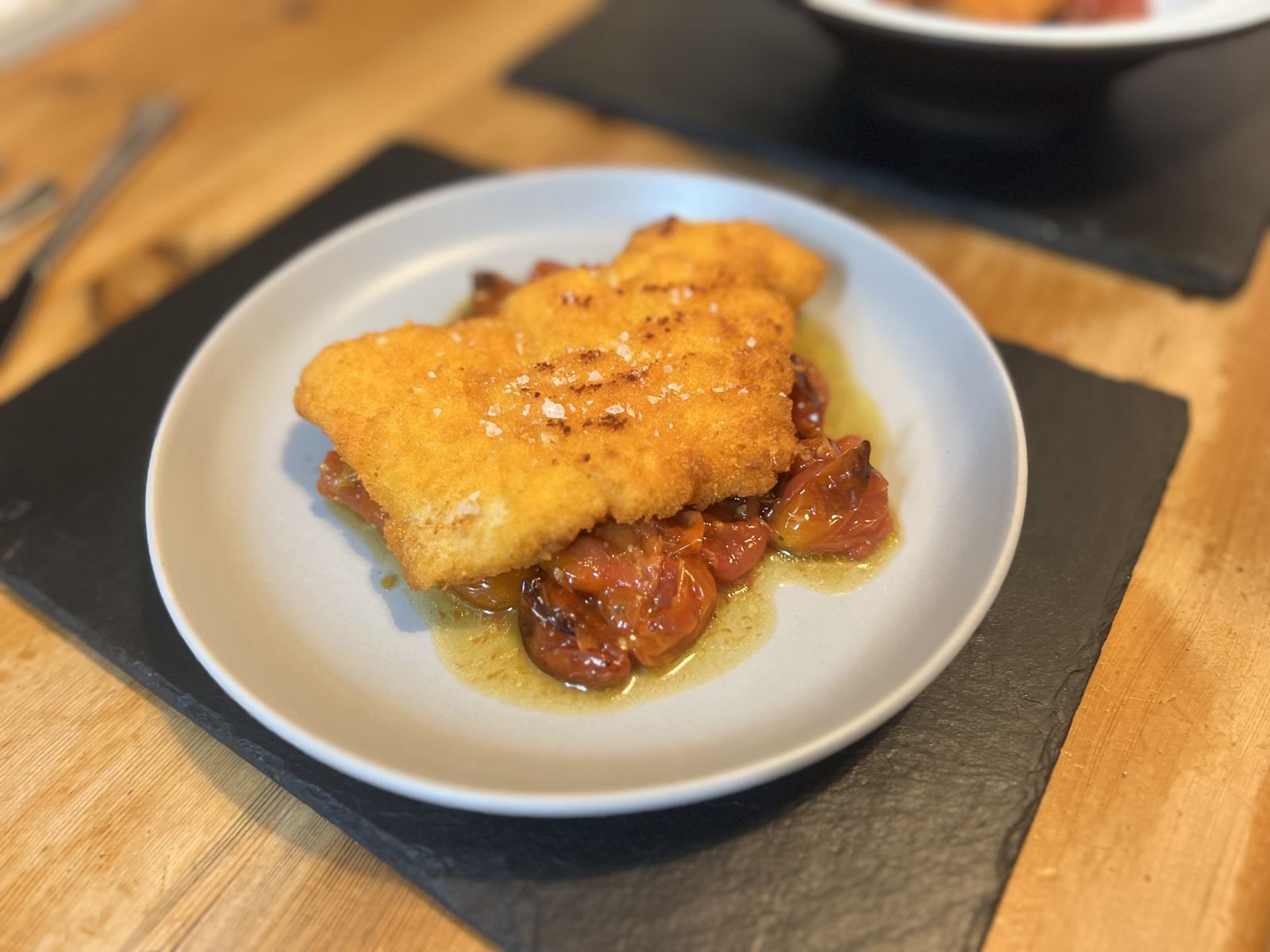Golden crumbed cod schnitzel on slow-roasted tomatoes